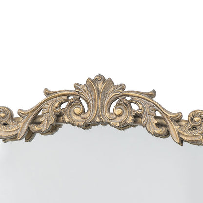 Gold mirror leaning against wall with plant and furniture